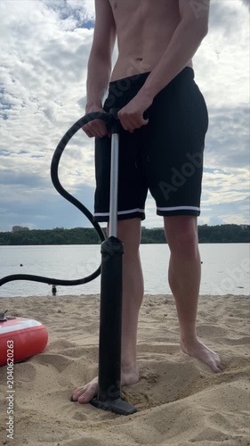 A close-up of a guy pumping up a SUP board on a river bank, an active sports lifestyle in the summer, SUP board,