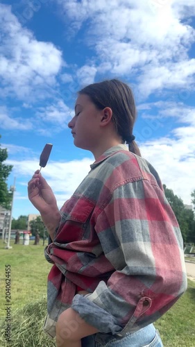 happy child eats ice cream while relaxing in the park on a summer day, girl 11 years old with dark hair eats colorful ice cream, having fun in the amusement park