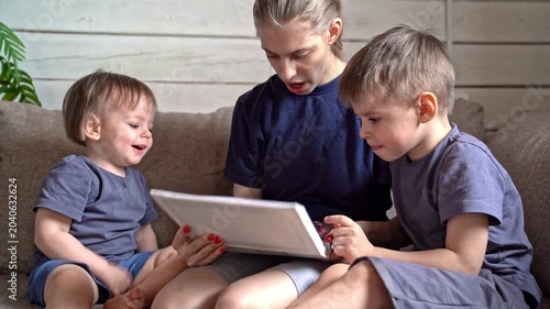 White tutor showing pictures to two white boys on couch, close hands pointing at illustrations, neutral wooden wall and plant, quiet focused atmosphere of early learning and gentle exploration