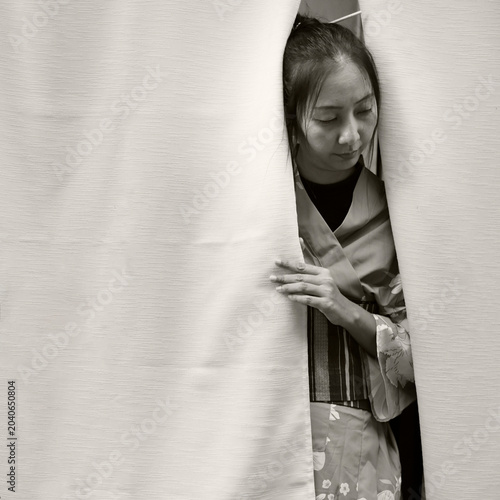 Japanese woman in blue floral kimono peeking through white noren curtain, in sepia black and white, Kyoto, Japan