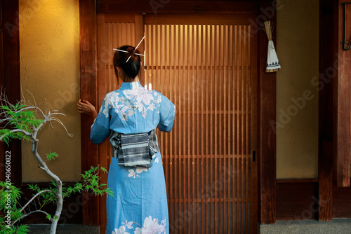 Woman in blue floral kimono standing at traditional wooden sliding door, Kyoto, Japan