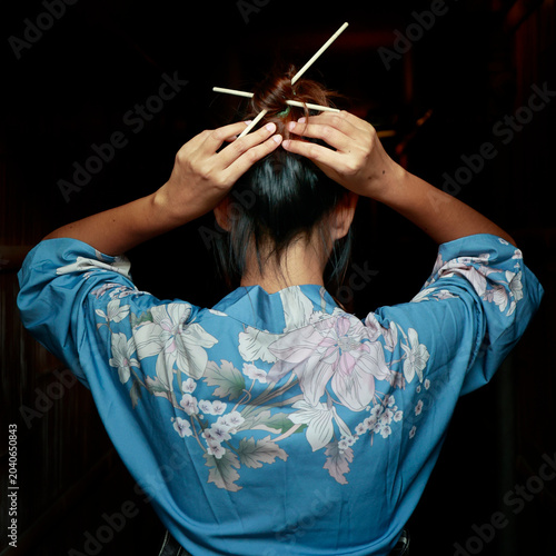 Woman in blue floral kimono arranging hair with kanzashi hairpins, rear view, Kyoto, Japan