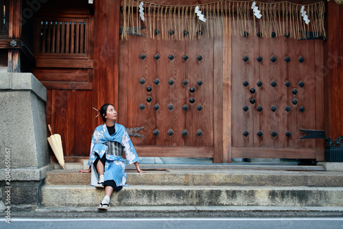 Young Woman in Blue Kimono Sitting on Steps of Japanese Shrine Gate