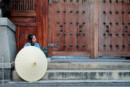Young Woman in Blue Kimono Behind Paper Umbrella at Japanese Shrine Gate