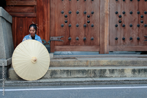 Young Woman in Blue Kimono Behind Paper Umbrella at Japanese Shrine Gate