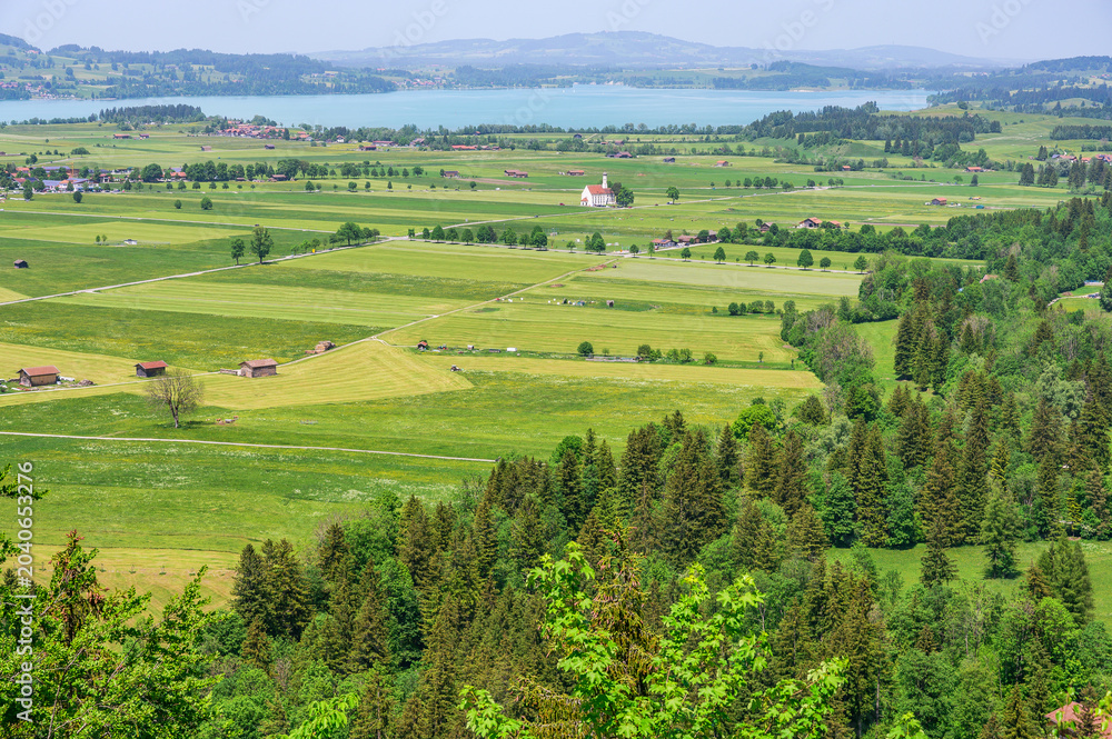 Obraz premium Scenic Bavarian landscape with rolling green fields, a lake, and distant mountains