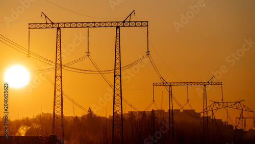 Silhouetted power lines stretch across the warm orange sky