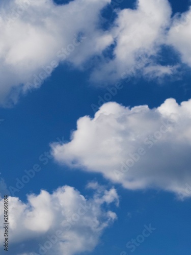 Beautiful fluffy white cumulus clouds scattered across a deep blue sky on a bright sunny day. Natural sky background template with copy space