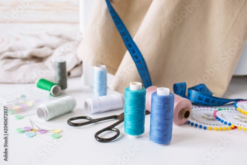 Sewing supplies on a white table with a sewing machine in the background. Sewing machine with fabric and sewing accessories on a white table.