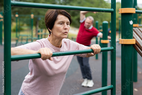 Photography elderly woman performs exercises on horizontal bars in an outdoor sports area