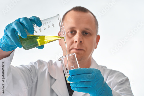 Lab scientist, pouring yellow liquid sample from larger to smaller beaker, closeup detail