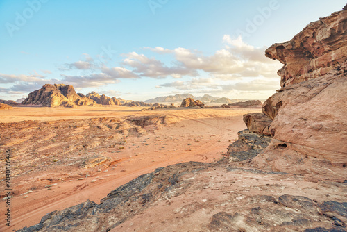 Red orange rocks and sand landscape of Wadi Rum desert lit by afternoon sunlight