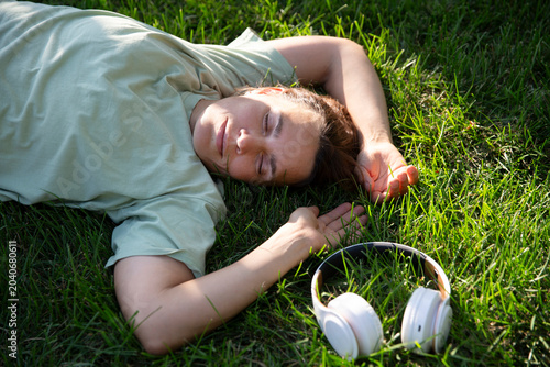 Audio healing. meditation. Slow life. Enjoying the little things. Dreaming of spring. middle aged woman wearing headphones listens to music lying on the grass on a spring day. 