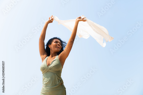 Happy black woman holding flowing scarf on the beach