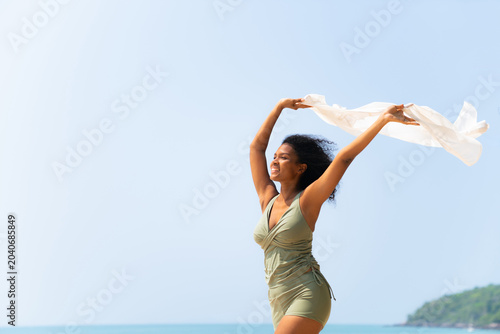 Happy black woman holding flowing scarf on the beach