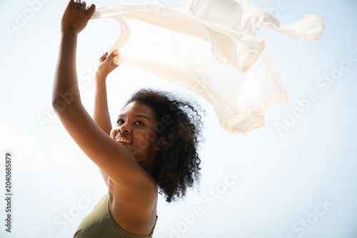Happy black woman holding flowing scarf on the beach