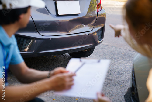 Woman pointing at car damage to insurance agent at roadside