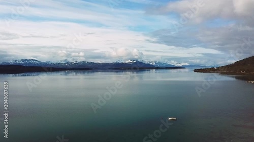A wide view shows islands surrounded by water with mountains and trees in the background. The sun is shining and the sky is mostly clear. This area is located in Norway.