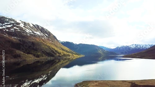 A wide view shows islands surrounded by water with mountains and trees in the background. The sun is shining and the sky is mostly clear. This area is located in Norway.