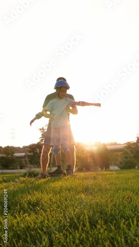 Father teaches son roller skating in park. Child practices balance on skates under sunny sky. Vertical composition capturing skill development, mentorship and active learning outdoors.