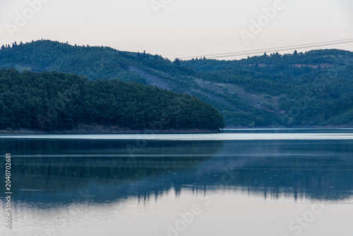 Bild auf Leinwand Tranquil landscape of Lake Plastira in Greece featuring forested mountains softly reflecting on the calm, mirror-like water surface