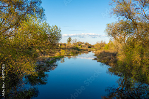 Quadro em tela A wide, tranquil river acts as a mirror for the vibrant blue sky and soft white