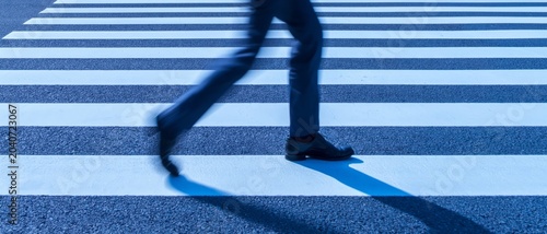 Person's legs in motion crossing a modern city crosswalk with motion blur