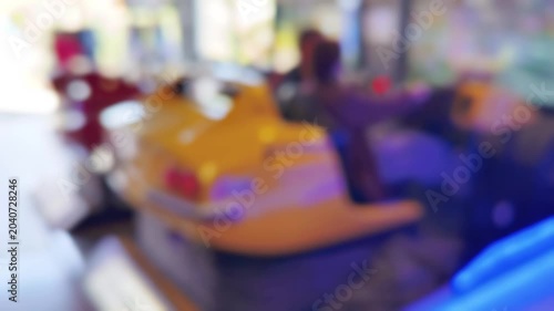 Defocused bokeh of yellow arcade racing game cabinet with vibrant neon lights and colorful screens. Dreamy out-of-focus aesthetic captures retro gaming atmosphere and entertainment venue energy.
