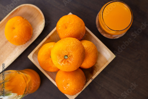 Fresh orange juice in a glass served with a whole ripe orange and a halved one on a wooden plate, view from above