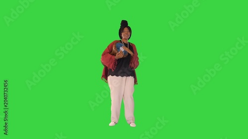 Cheerful african american woman in traditional clothes beats djembe drum and dances on a Green Screen, Chroma Key.