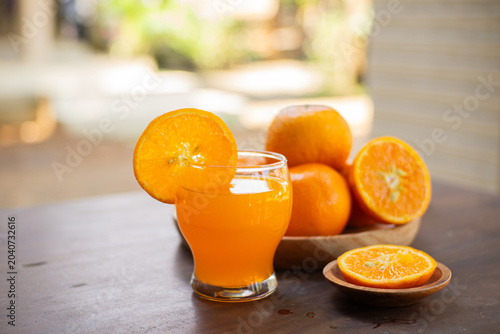 Fresh cut oranges on a wooden plate with a bottle and a glass of fresh orange juice on a outdoor table