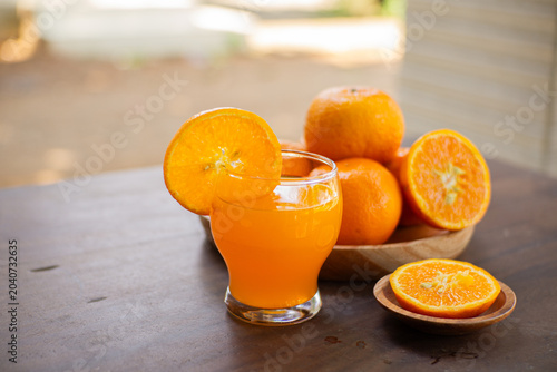 Fresh cut oranges on a wooden plate with a bottle and a glass of fresh orange juice on a outdoor table