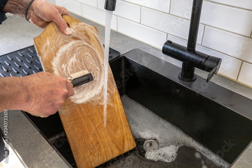 Obraz na plátne Stockholm, Sweden A man scrubs a wooden kitchen cutting board with soap and water