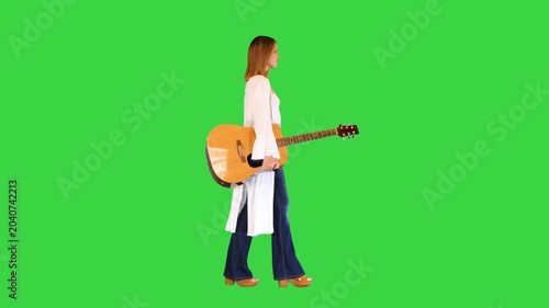 Beautiful young woman walking around with an acoustic guitar on a Green Screen, Chroma Key.