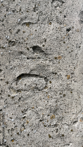 Foto A close-up, full-frame texture of a rough, heavily weathered gray concrete surface featuring deep indents, craters, and scattered small patches of yellow and white lichen
