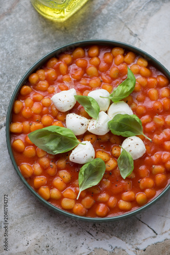 Plate with mini potato gnocchi in tomato sauce, mozzarella and green basil, vertical shot on a grey granite background, middle close-up