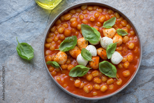 Plate of italian chicche di patate in tomato sauce with mozzarella balls and basil, horizontal shot on a beige and blue granite background, high angle view