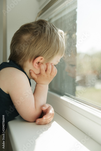 Curious little boy looking through a window at home. Childhood, curiosity, waiting, imagination, family life and cozy home lifestyle concept.