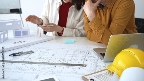 Architects collaborating on building design, analyzing blueprints and a scale model, planning future construction project development with digital tools in an office
