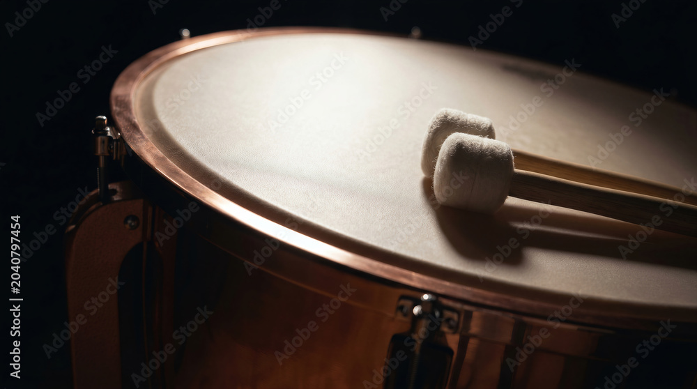 Obraz premium Close up of orchestral timpani drum with mallets on professional percussion instrument on dark background.