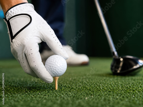A golfer wearing a white glove placing a golf ball on a wooden tee on a green grass field ready to hit a shot