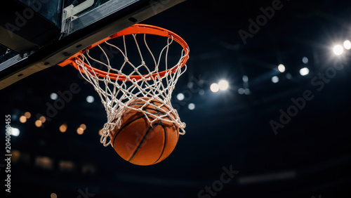 Basketball ball going through the net during a professional match in a dark indoor arena with bright stadium lights