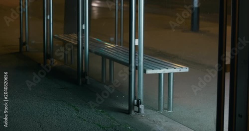 Empty bench inside a glass bus stop shelter in Zagreb Croatia at night.