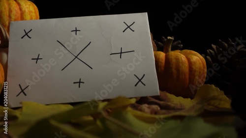 Autumn still life pumpkins on tabletop soft warm light, assorted gourds and leaves arranged over burlap, white notecard marked with crosses and plus signs, dark backdrop creating dramatic shadows,