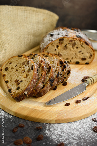 Homemade raisin walnut bread dusted with powdered sugar on a wooden board with a sieve, vintage knife and burlap, rustic bakery still life