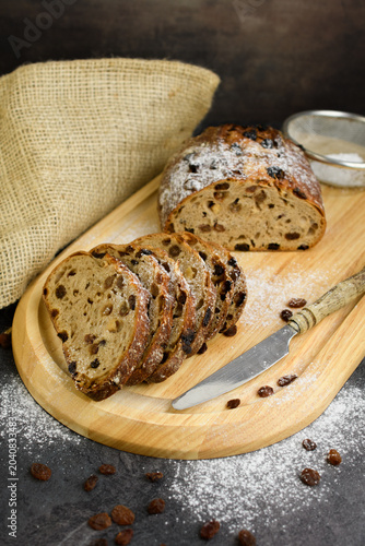 Homemade raisin walnut bread dusted with powdered sugar on a wooden board with a sieve, vintage knife and burlap, rustic bakery still life