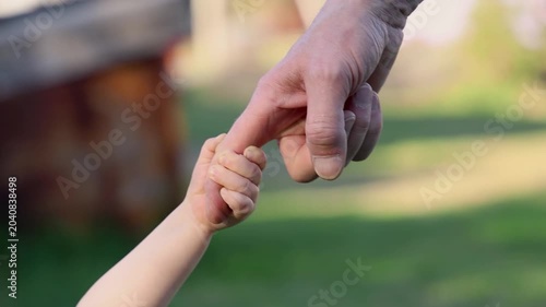 A toddler walks hand in hand with his father, close-up