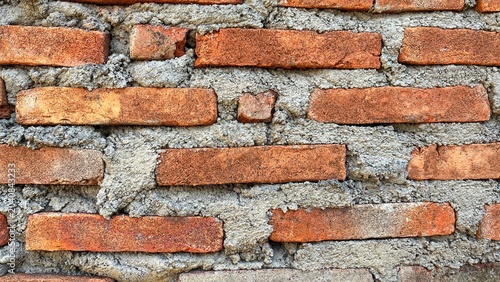 Quadro su tela Close-up texture of a traditional red brick wall with rough cement mortar joints