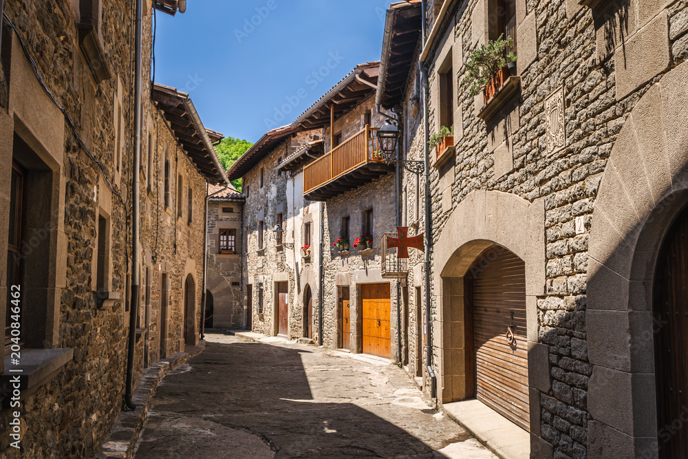 Fototapeta premium Narrow medieval street lined with traditional stone houses in Rupit village, Catalonia, Spain, featuring rustic architecture