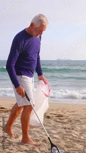 Mature 66 year old man picking up trash from a beach in Southern California. Vertical Video.